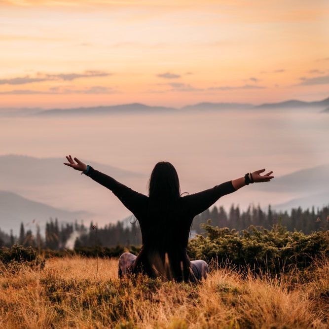 Yoga woman sitting on top of a mountain at sunrise.